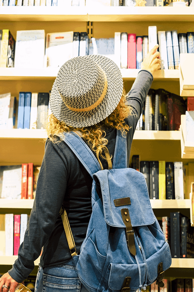Woman with backpack and straw hat selecting a book from book store shelves
